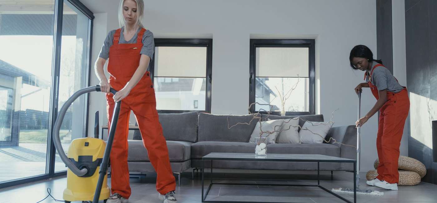 Two uniformed cleaners vacuuming and mopping a living room