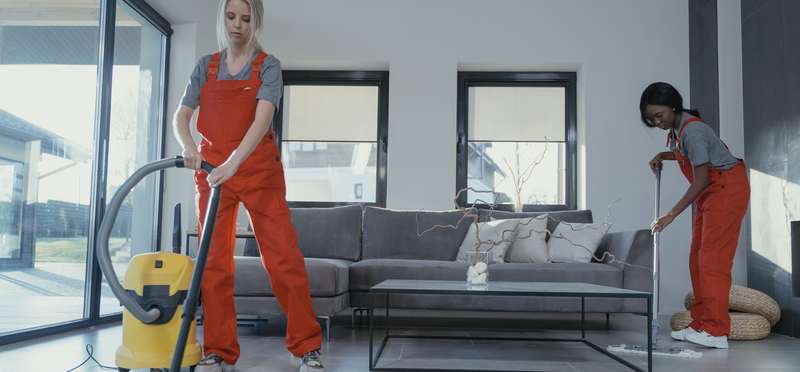 Two uniformed cleaners vacuuming and mopping a living room