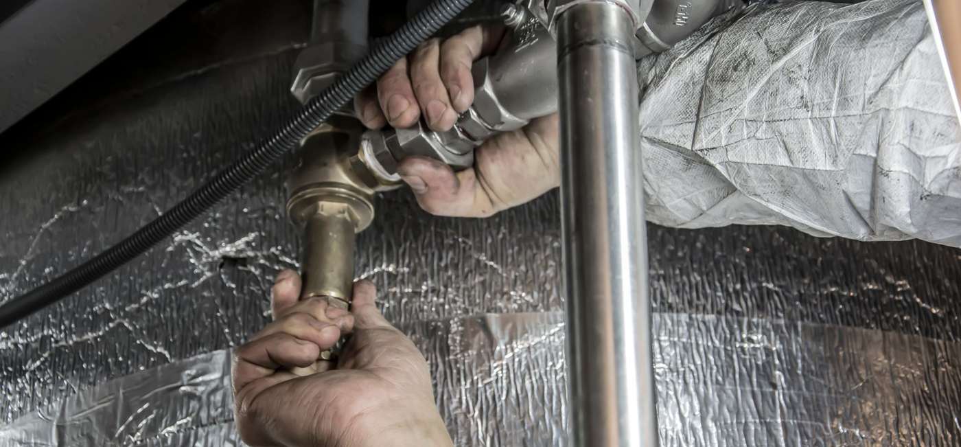 A plumber&rsquo;s hands fitting steel pipe beneath a floor