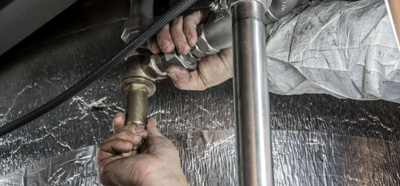 A plumber&rsquo;s hands fitting steel pipe beneath a floor